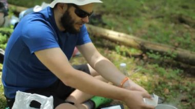 Ormanda gaz brülöründe tencerede yemek hazırlayan bir adam. Yerde oturup çorbayı karıştır.