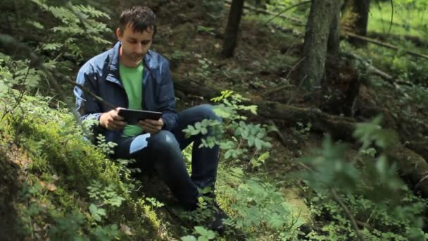 L'homme dans la tablette Forest Touch. Il est assis sur une petite falaise verte — Video