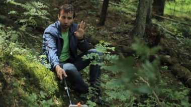 Ormandaki adam telefonda selfie çubuklarıyla fotoğraf çekti. Küçük bir uçurumun üzerinde yeşil oturur