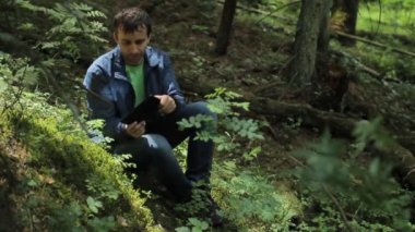 Ormandaki adam oyunda tablette oynuyor. Küçük bir uçurumun üzerinde yeşil oturur