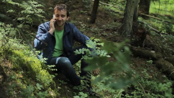 L'homme dans la forêt appelle par smartphone. Il est assis sur une petite falaise verte — Video