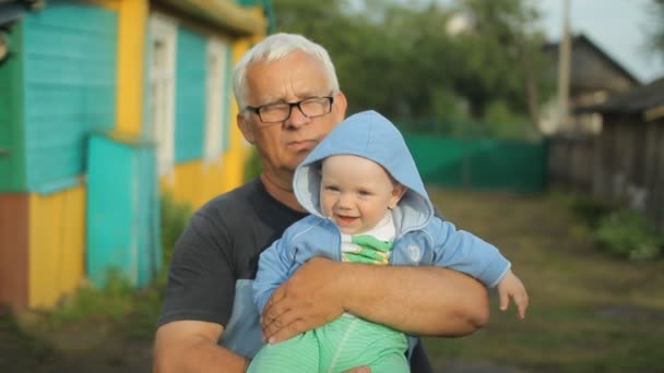 Grootvader houdt zijn kleinzoon in zijn armen. Mooie baby glimlachend — Stockvideo