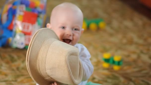 Schönes Baby versucht, seinen Hut zu essen. Der Junge ist weniger als ein Jahr alt — Stockvideo