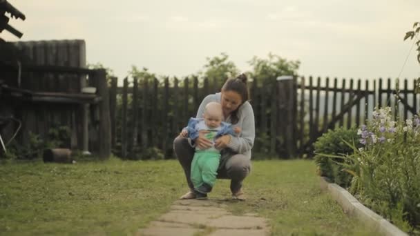 Gyönyörű baba veszi az első lépéseket az anyjával. Mennek le az út ház — Stock videók