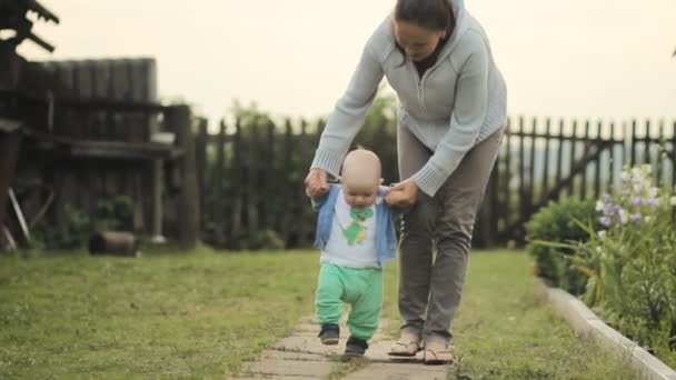 Bebê bonito dá seus primeiros passos com sua mãe. Eles descem a cabana do caminho — Vídeo de Stock