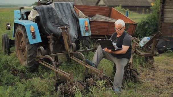 Um homem a trabalhar num portátil perto do tractor e a afastar-se. Agricultura circundante — Vídeo de Stock