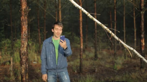 남자는 숲에 있는 나무 근처 전화 화상 통화를 만든다. 이른 아침 — 비디오