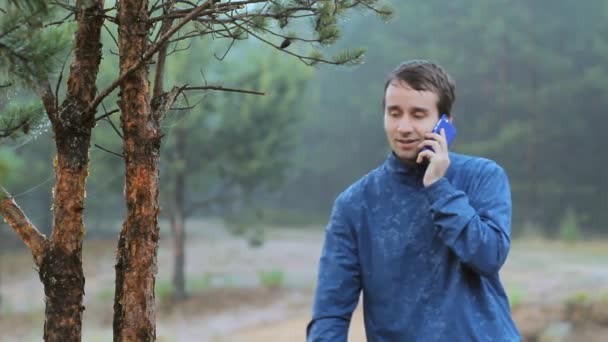 Um homem a ligar ao telefone perto de uma árvore na floresta. De manhã cedo — Vídeo de Stock