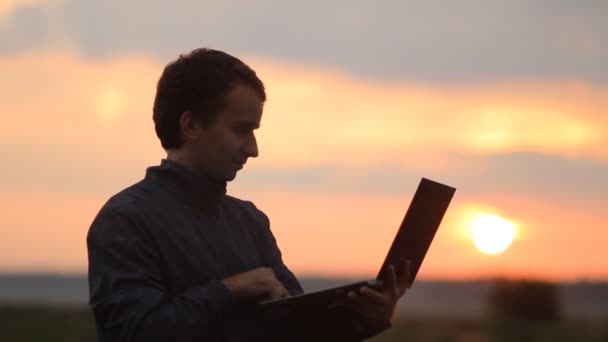 Un hombre hace una videollamada en un portátil. Hermosa puesta de sol en el fondo — Vídeo de stock