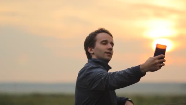 Mannen gör fotot på den smarta telefonen. Vacker solnedgång i bakgrunden — Stockvideo
