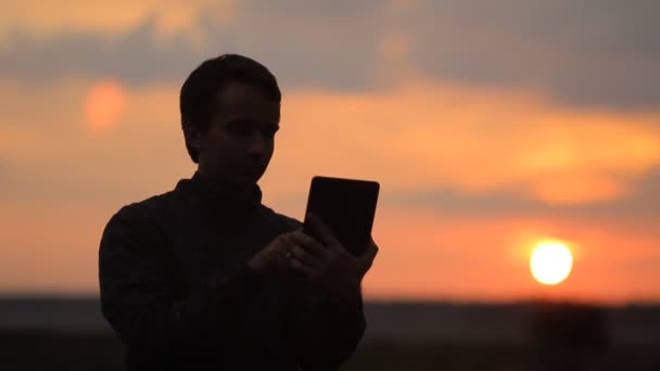 O homem toca no tablet. Belo pôr do sol no fundo — Vídeo de Stock