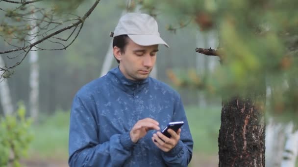 L'uomo compone sms al telefono vicino a un albero nella foresta. La mattina presto — Video Stock