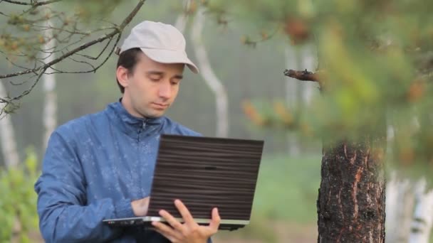 Человек, работающий на ноутбуке возле дерева в лесу. Ранним утром — стоковое видео