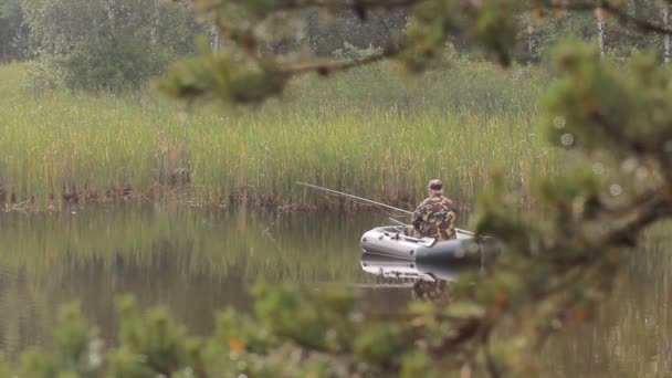 En fiskare i en båt med ett fiskespö som väntar på fisken. Tidiga morgondimman vid sjön — Stockvideo