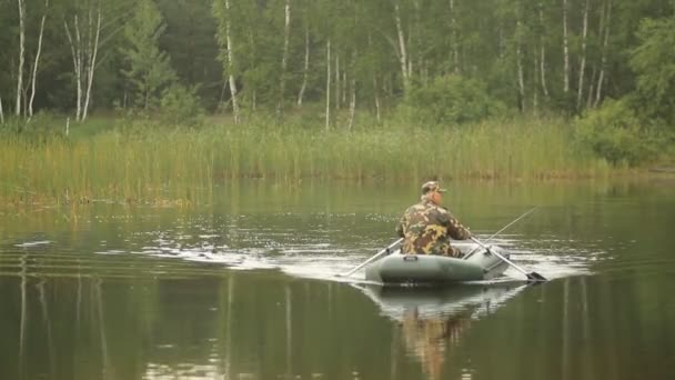 Hombre pescador flota en un lago en un barco inflable. Temprano. — Vídeos de Stock