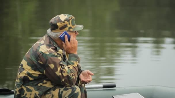 Pria yang menelepon lewat telepon di danau. Seorang nelayan dengan tongkat pancing di perahu karet — Stok Video