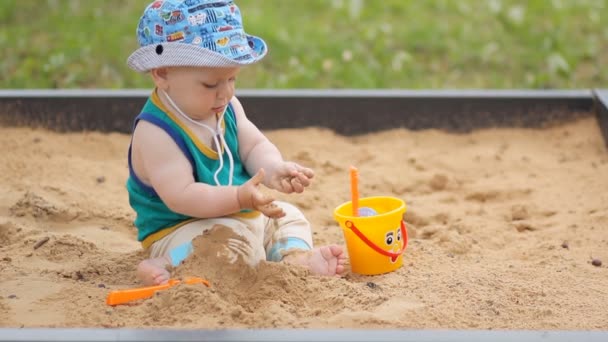 Babyjongen graven in de zandbak. Glimlacht en raakt het zand — Stockvideo