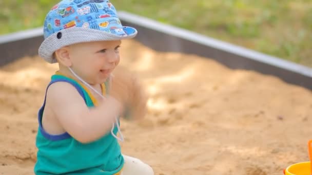 Baby boy digging in the sandbox. Smiles and touches the sand — Stock Video