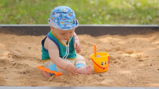 Babyjongen graven in de zandbak. Glimlacht en raakt het zand — Stockvideo