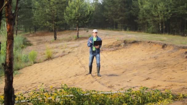 En man i stövlar gå på en sandstrand med laptop — Stockvideo