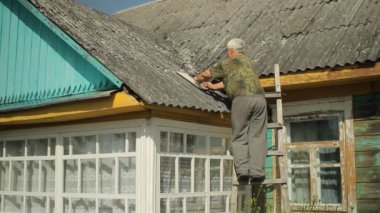Bir adam çatı gidermeye çalışır. O merdivenlerde evin yanında duruyor