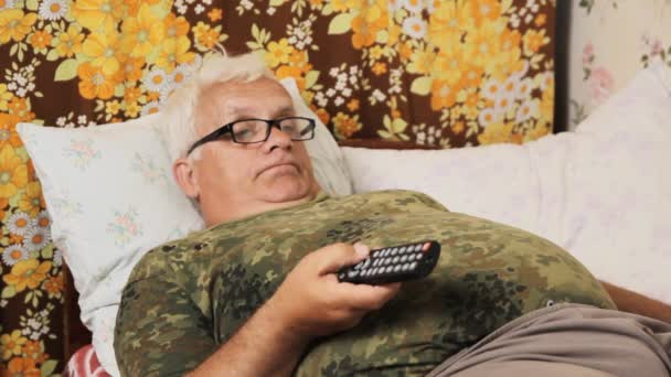 Senior mannen i sängen hemma med TV-fjärrkontrollen — Stockvideo