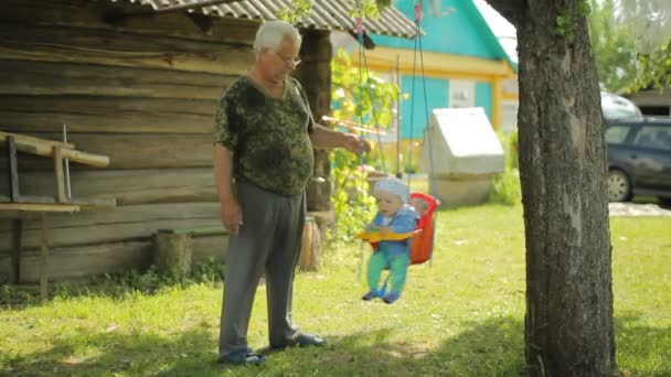 L'uomo più anziano fa rotolare il bel bambino su un'altalena. Nonno con suo nipote nel giardino della sua casa — Video Stock