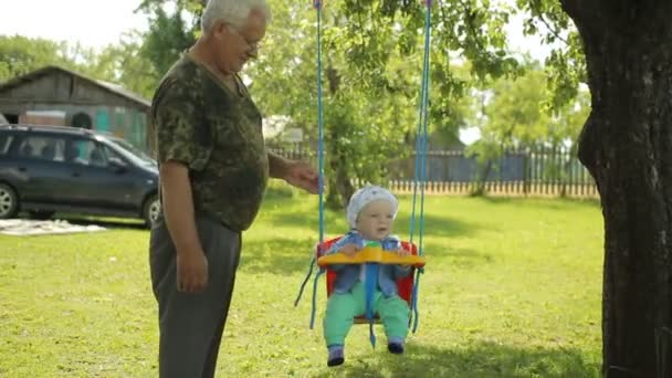 El hombre mayor enrolla al hermoso bebé en un columpio. Abuelo con su nieto en el jardín de su casa — Vídeo de stock