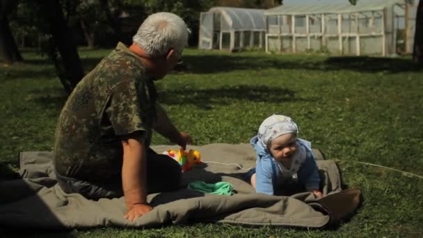 Счастливые дедушка и внук лежат на траве. Мбаппе меньше года — стоковое видео