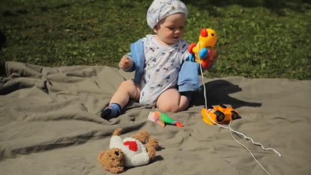Şirin oynak sarışın 1 yıl yaşlı çocuk yeşil üzerinde oturan çim açık oyuncakları ile oynarken gülümsedi — Stok video