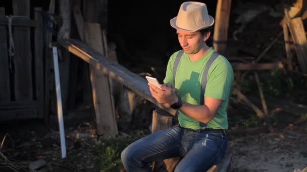 Молодой человек делает видеозвонок на закате. Мужчина сидит на лесопилке — стоковое видео