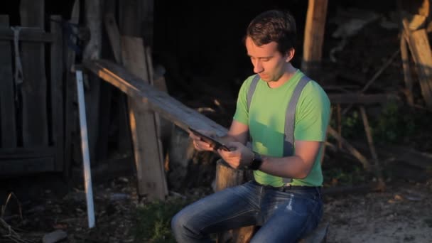 Een man spelen op een tablet bij de zagerij. zonsondergang tijd — Stockvideo