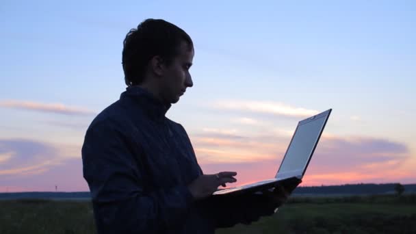 Νεαρός άνδρας είναι χαλαρωτικό σε εξωτερικούς χώρους με φορητό υπολογιστή στα χέρια του — Αρχείο Βίντεο
