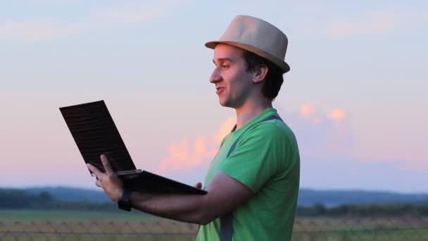 El joven se relaja al aire libre con la computadora portátil en sus manos — Vídeos de Stock