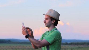 Bir adam telefonda görüntülü arama yapar. Güzel bir gün batımı gökyüzü fonunda