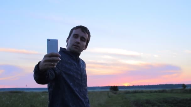남자는 전화 selfie를 만든다. 아름 다운 일몰 하늘 배경 — 비디오