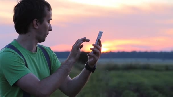 Fiatal férfi tartja a mobilját, naplementekor. Írj SMS-t — Stock videók