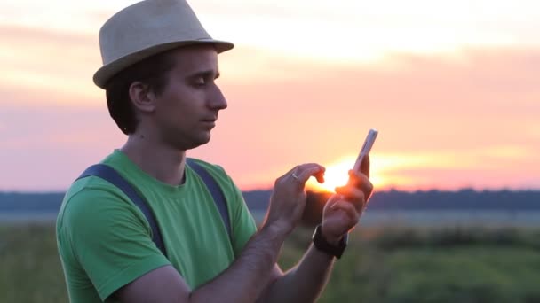 Ung man innehar en mobiltelefon vid solnedgången. Han skriva sms — Stockvideo