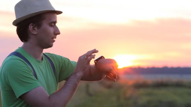 Hombre tocando reloj inteligente en el fondo del cielo hermoso atardecer — Vídeo de stock