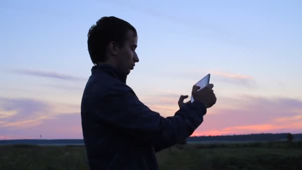 Un hombre jugando en una tablet en el juego. Sobre el telón de fondo de un hermoso cielo al atardecer — Vídeos de Stock