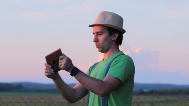 Un hombre jugando en una tablet en el juego. Sobre el telón de fondo de un hermoso cielo al atardecer — Vídeos de Stock