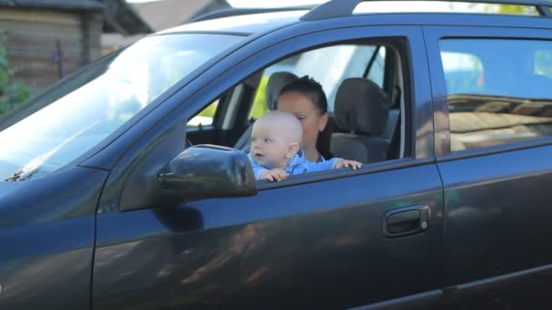 Мати з дитиною сидить у машині на сидінні водіїв. Дитина грає посміхаючись — стокове відео