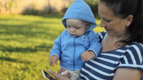 Un bambino tenuto in braccio dalla madre nel parco. Mamma chiama al telefono. . — Video Stock