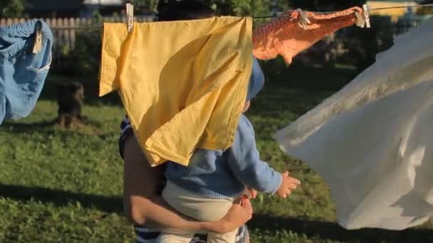 Mother with beautiful baby walks in the summer garden. One considers as drying clothes on a rope — Stock Video