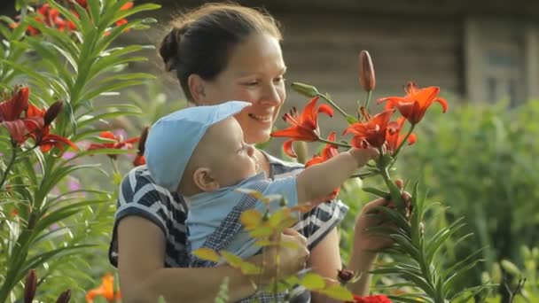 Tânăra mamă cu băiatul ei frumos atingând flori lângă casa lui. Fiul se uită atent la plante. — Videoclip de stoc