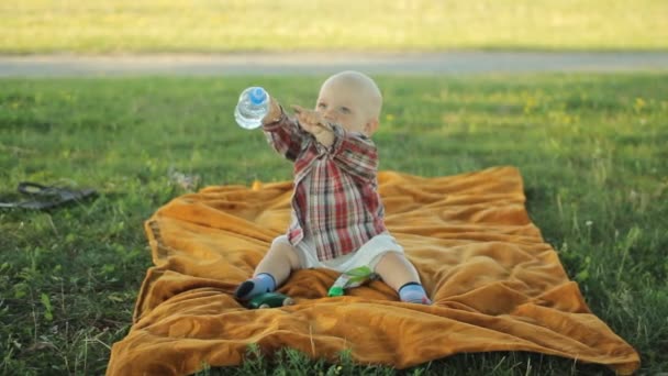 Schattige kleine jongen, zittend op een deken in het park. Baby minder dan een jaar en hij speelde — Stockvideo