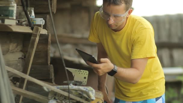 A man working on a tablet, puts aside tablet and begins sawing metal with angule grinder. Flying sparks — Stock Video