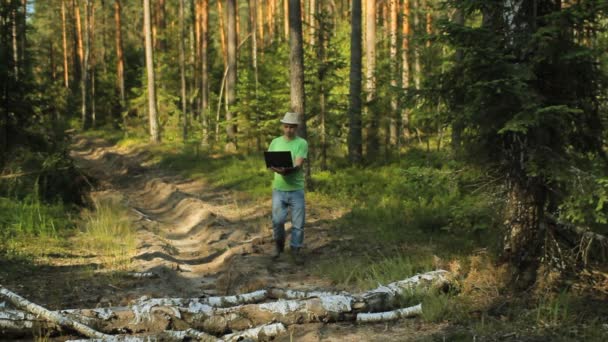 Un hombre camina por el bosque con una computadora portátil y mirando el mapa elige la dirección correcta — Vídeo de stock