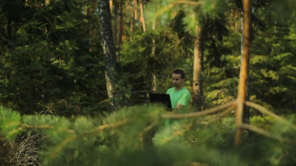 Um homem caminha pela floresta com um laptop e olhando mapa Ele escolhe a direção certa — Vídeo de Stock