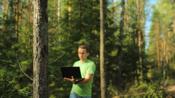 Um homem caminha pela floresta com um laptop e olhando mapa Ele escolhe a direção certa — Vídeo de Stock